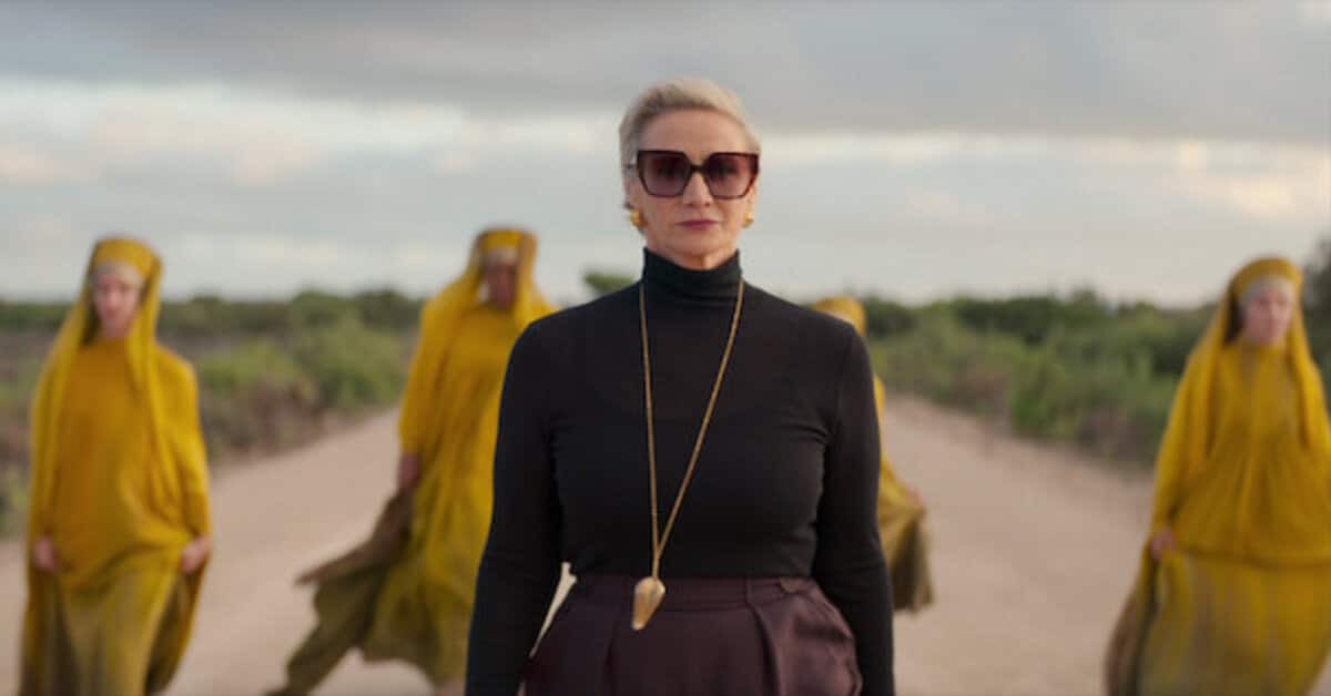 Descrição da imagem: mulher branca e loira na frente de quatro mulheres negras vestidas com trajes amarelos da mitologia grega. Divulgação Netflix.